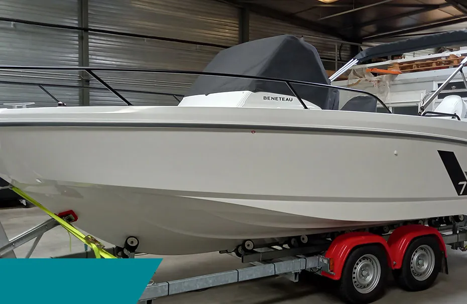 Bateau à moteur Bénéteau blanc posé sur une remorque à double essieu dans un atelier.