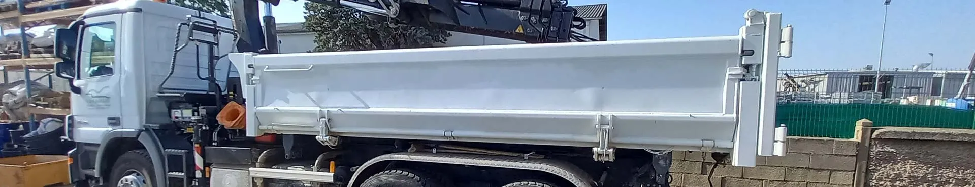 Camion-benne blanc à trois essieux équipé d’une grue auxiliaire.