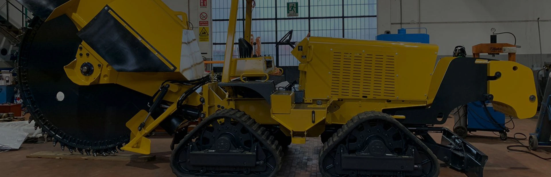 Machine industrielle jaune sur chenilles avec une grande roue de coupe dans un atelier.