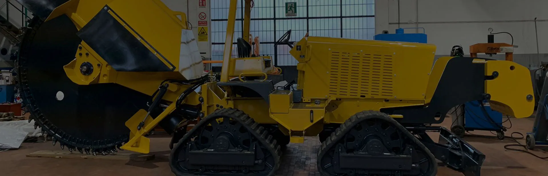 Machine industrielle jaune sur chenilles avec une grande roue de coupe dans un atelier.