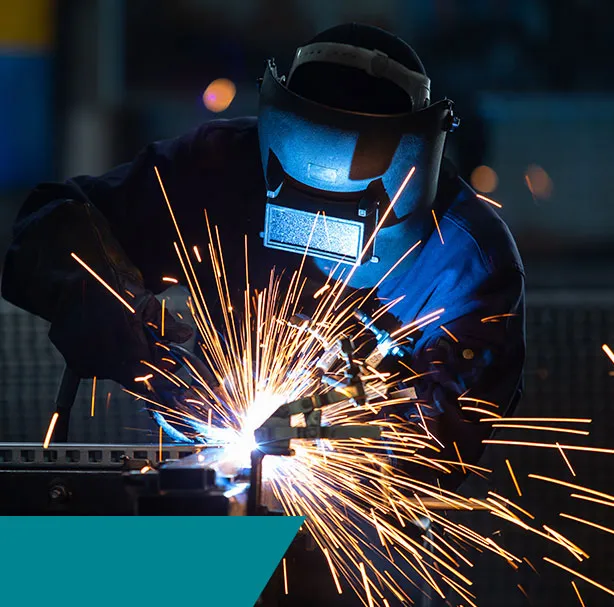 Soudeur casqué travaillant une pièce métallique au milieu d’étincelles dans un atelier.