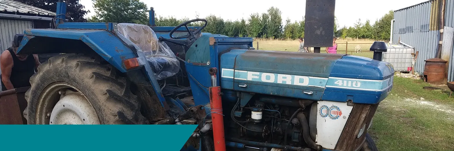 Tracteur agricole bleu Ford 4110 photographié de profil dans une cour.