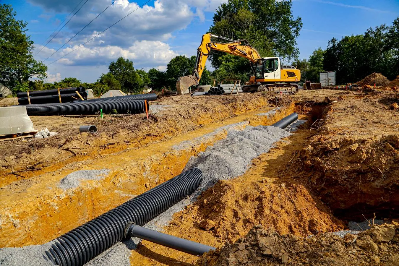 Pelle hydraulique jaune et canalisations noires sur un chantier en extérieur.